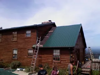 Green metal roof going on a two story log home with ladders set in Battle Ground